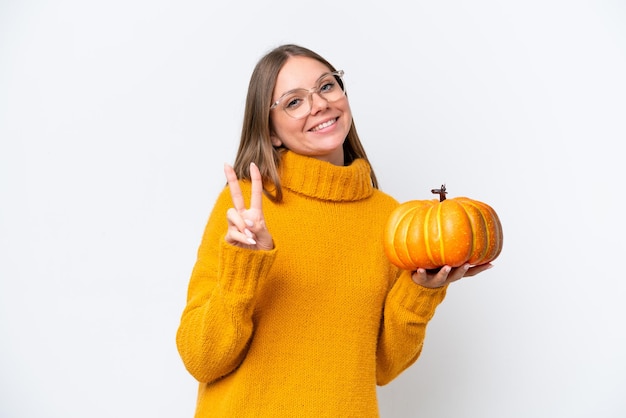 Young caucasian woman holding a pumpkin isolated on white background smiling and showing victory sign