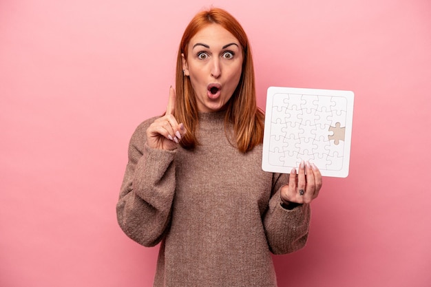 Young caucasian woman holding puzzle isolated on pink background having some great idea concept of creativity