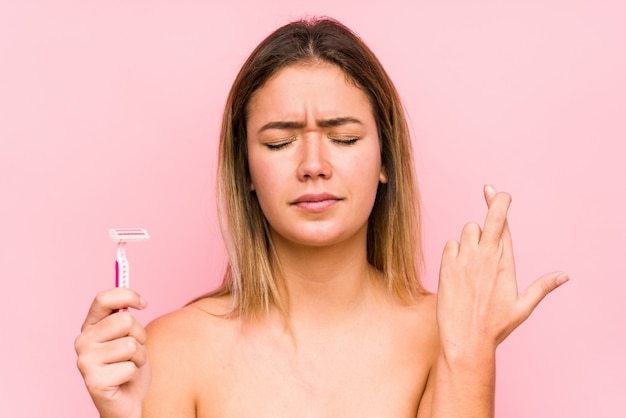 Young caucasian woman holding a razor and crossing fingers for having luck