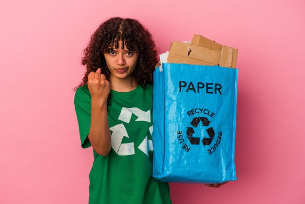 Young caucasian woman holding a recycled plastic isolated on pink background showing fist to camera, aggressive facial expression.