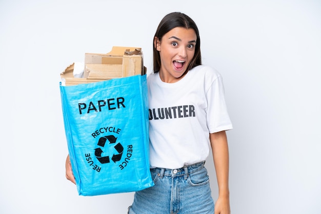 Young caucasian woman holding a recycling bag full of paper to recycle isolated on white background with surprise and shocked facial expression