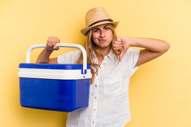 Young caucasian woman holding refrigerator isolated on yellow background  showing a dislike gesture, thumbs down. Disagreement concept.