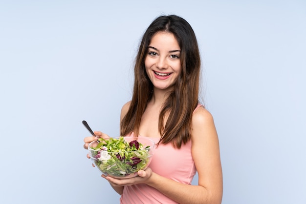 Young caucasian woman holding a salad on blue wall