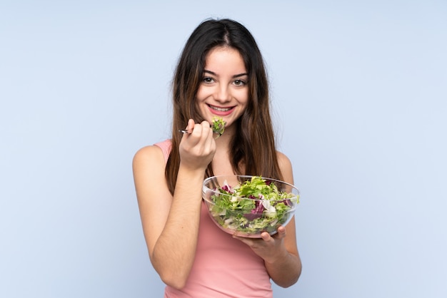 Young caucasian woman holding a salad isolated on blue
