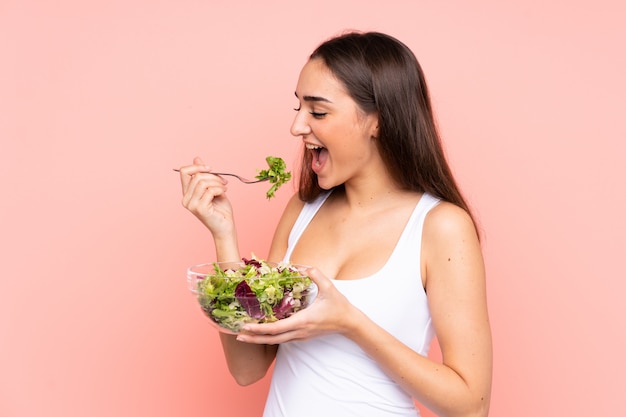 Young caucasian woman holding a salad isolated on pink wall