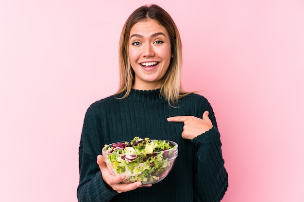 La giovane donna caucasica che tiene un'insalata isolata ha sorpreso indicare se stesso, sorridendo ampiamente.