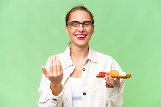 Foto giovane donna caucasica che tiene il sashimi su sfondo isolato che invita a venire con la mano felice che tu sia venuto