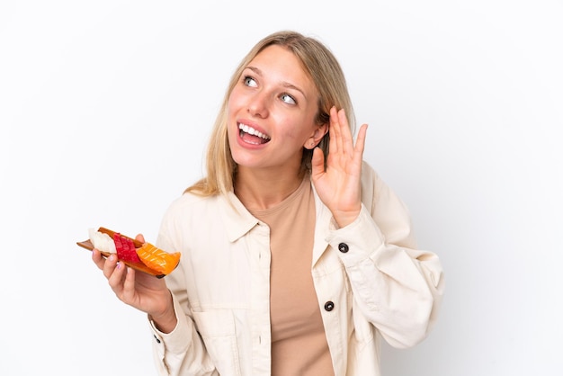 Young caucasian woman holding sashimi isolated on white background listening to something by putting hand on the ear