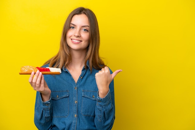 Young caucasian woman holding sashimi isolated on yellow background pointing to the side to present a product