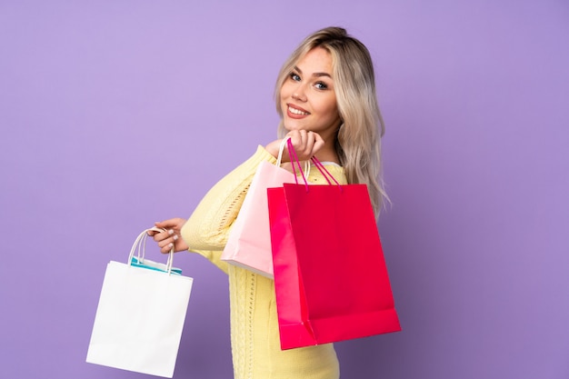 Young caucasian woman holding shopping bags over purple wall