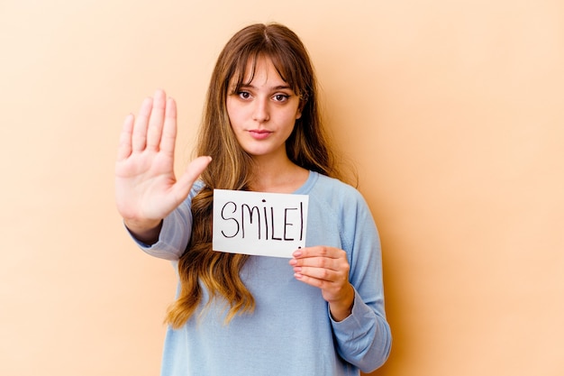 Young caucasian woman holding a Smile placard isolated standing with outstretched hand showing stop sign, preventing you.