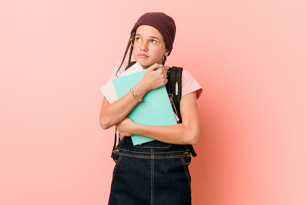 Young caucasian woman holding some notebooks looking sideways with doubtful and skeptical expression.