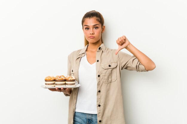 嫌いなジェスチャー、親指ダウンを示す甘いケーキを保持している若い白人女性。不一致の概念。