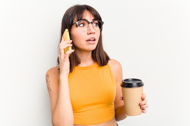 Giovane donna caucasica in possesso di un caffè da asporto e un telefono cellulare isolato su sfondo bianco