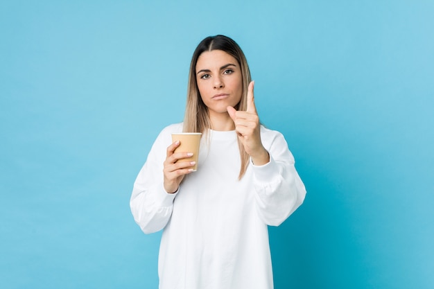 Young caucasian woman holding a takeaway coffee showing number one with finger.