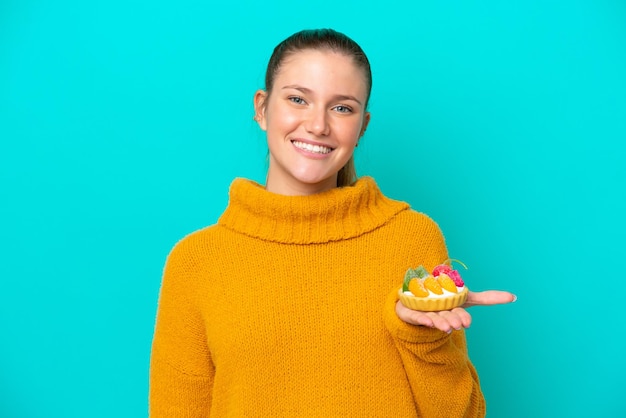 Young caucasian woman holding a tartlet isolated on blue background smiling a lot