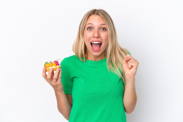 Young caucasian woman holding a tartlet isolated on white background celebrating a victory in winner position