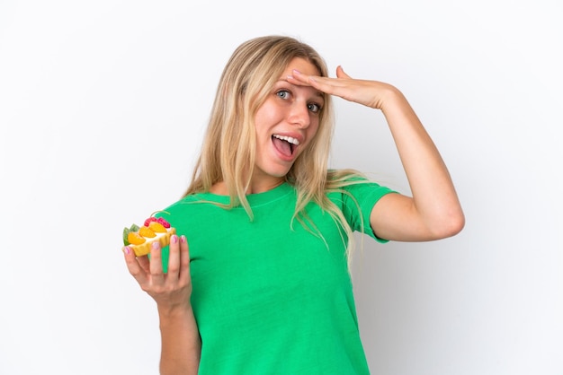 Young caucasian woman holding a tartlet isolated on white background doing surprise gesture while looking to the side