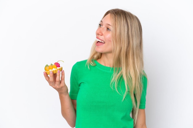 Young caucasian woman holding a tartlet isolated on white background laughing in lateral position