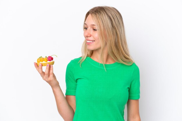 Young caucasian woman holding a tartlet isolated on white background looking side