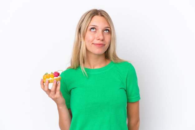 Young caucasian woman holding a tartlet isolated on white background and looking up