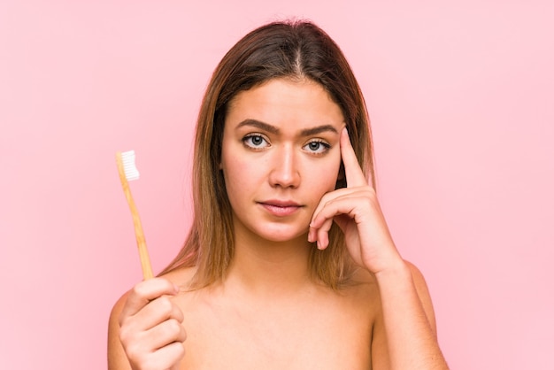 Young caucasian woman holding a teeth brush isolated pointing his temple with finger, thinking, focused on a task.