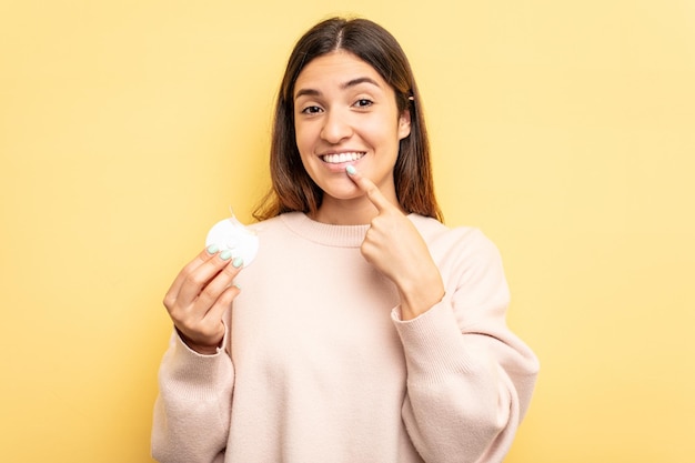 Young caucasian woman holding teeth whitener isolated on yellow background