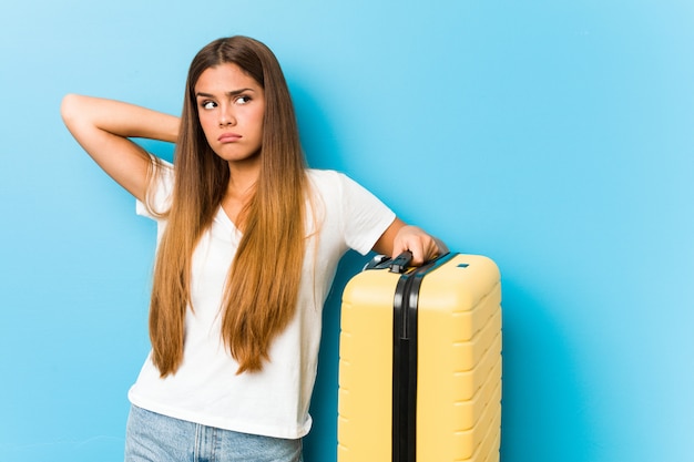 頭の後ろに触れる、考えて、選択をする旅行スーツケースを保持している若い白人女性。