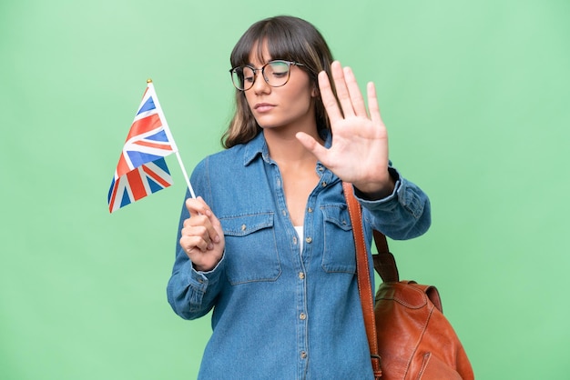 Young caucasian woman holding an united kingdom flag over isolated background making stop gesture and disappointed