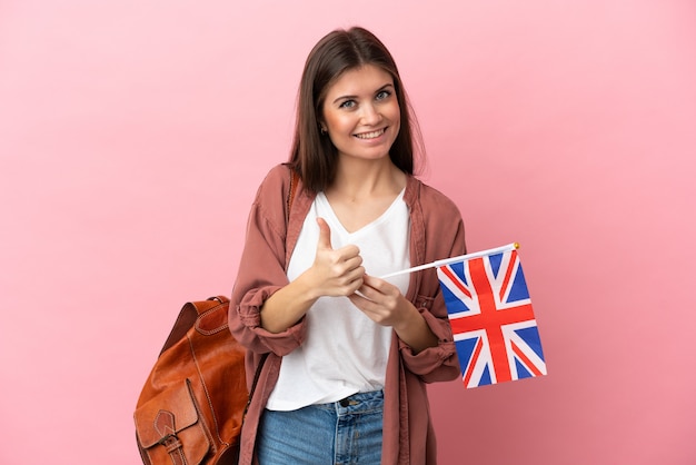 Young caucasian woman holding an United Kingdom flag isolated on pink background giving a thumbs up gesture