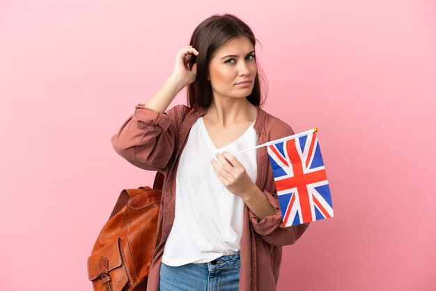 의심이 있는 분홍색 배경에 고립 된 영국 국기를 들고 젊은 백인 여자