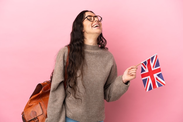 Young caucasian woman holding an United Kingdom flag isolated on pink wall laughing