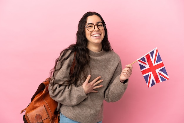 たくさん笑ってピンクの壁に分離されたイギリスの旗を保持している若い白人女性