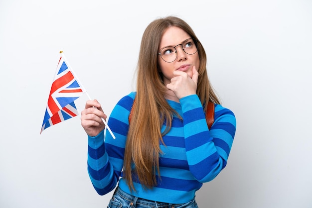 Young caucasian woman holding an United Kingdom flag isolated on white background having doubts