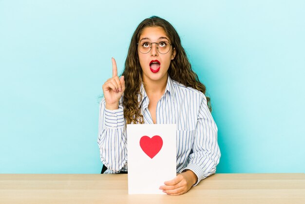 Young caucasian woman holding a valentines day card isolated pointing upside with opened mouth.