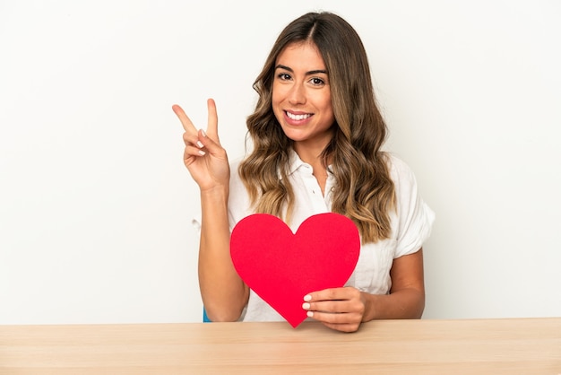 Young caucasian woman holding a valentines day heart isolated showing number two with fingers.