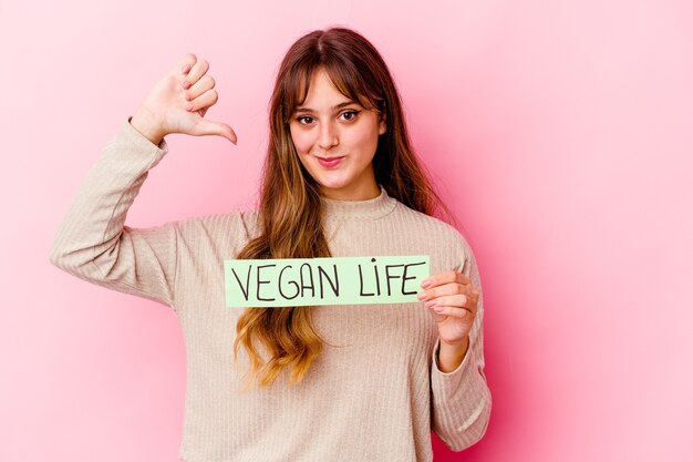 Young caucasian woman holding a vegan life placard feels proud and self confident, example to follow.