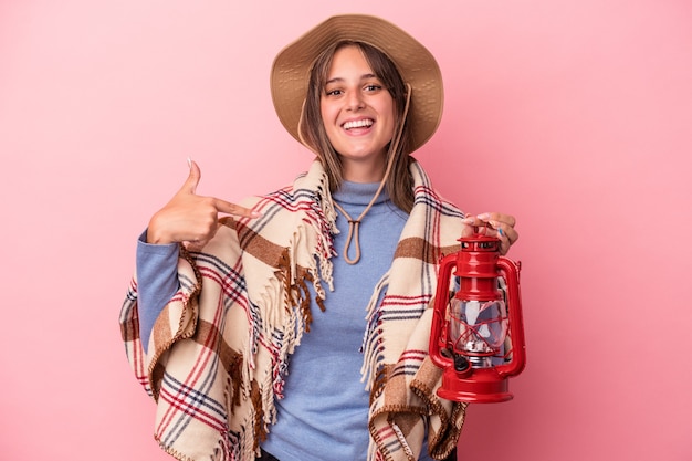 Young caucasian woman holding vintage lantern isolated on pink background person pointing by hand to a shirt copy space, proud and confident