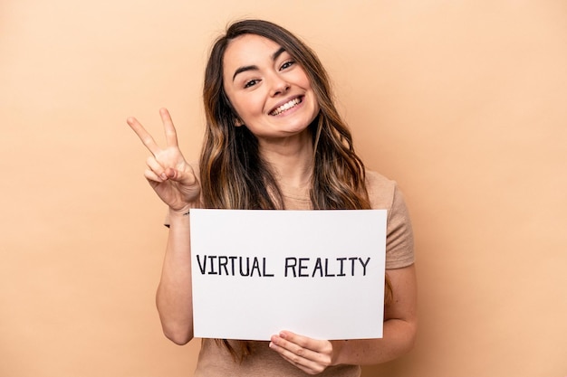 Young caucasian woman holding a virtual reality placard isolated on beige background joyful and carefree showing a peace symbol with fingers