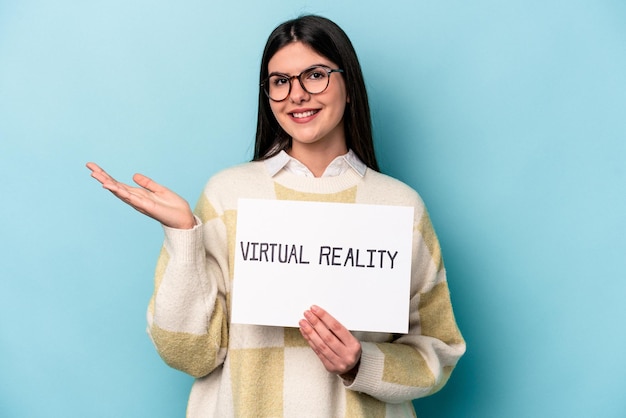 Young caucasian woman holding a virtual reality placard isolated on blue background showing a copy space on a palm and holding another hand on waist