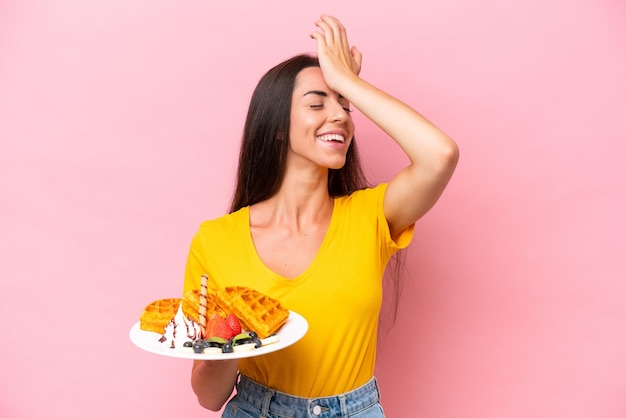 Young caucasian woman holding waffles isolated on pink background