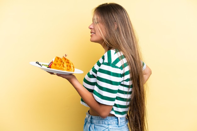 Young caucasian woman holding waffles isolated on yellow background suffering from backache for having made an effort