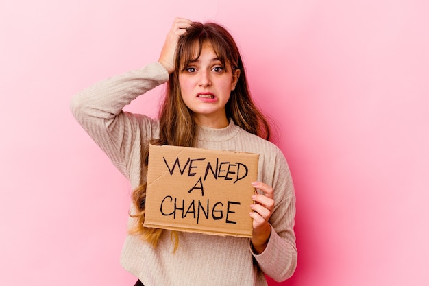 Young caucasian woman holding a We need a change placard isolated being shocked, she has remembered important meeting.