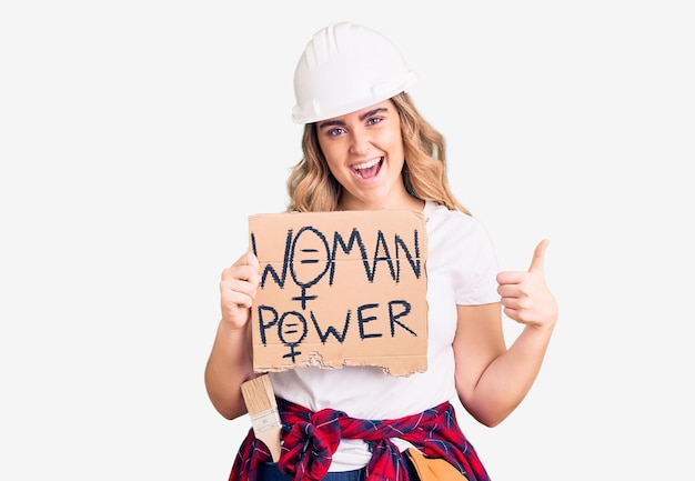 Young caucasian woman holding woman power banner smiling happy and positive thumb up doing excellent and approval sign