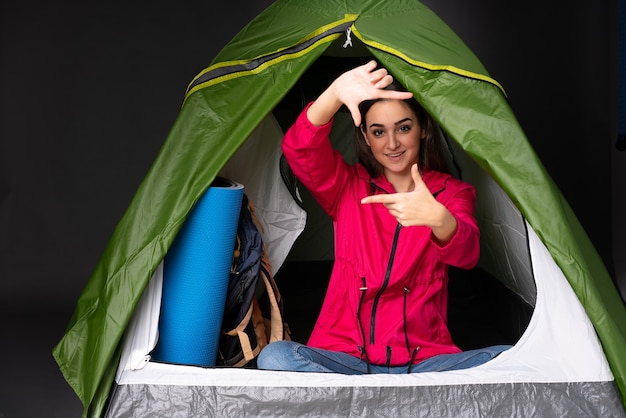 Молодая кавказская женщина в кемпинге зеленой палатки, фокусируя лицо