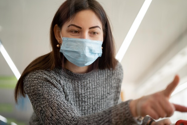 Young caucasian woman is shopping at the supermarket The medical mask is wearing points her finger at the desired food