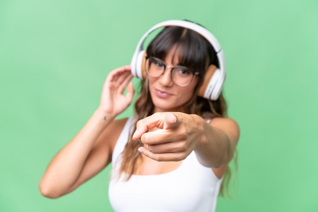 Photo young caucasian woman over isolated background listening music and pointing to the front