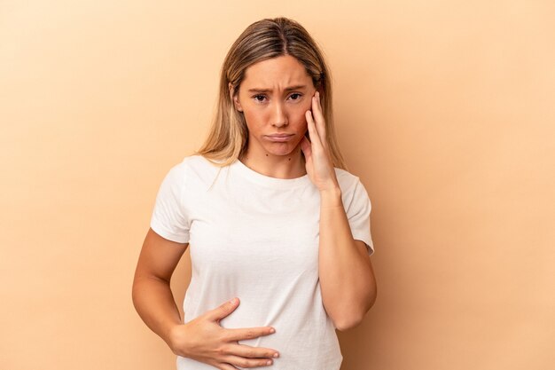 Young caucasian woman isolated on beige background blows cheeks, has tired expression. Facial expression concept.