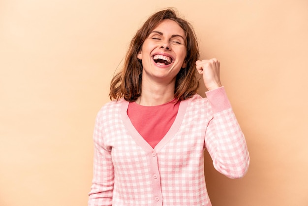 Young caucasian woman isolated on beige background celebrating a victory passion and enthusiasm happy expression