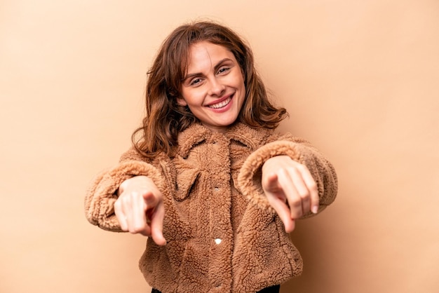 Young caucasian woman isolated on beige background cheerful smiles pointing to front